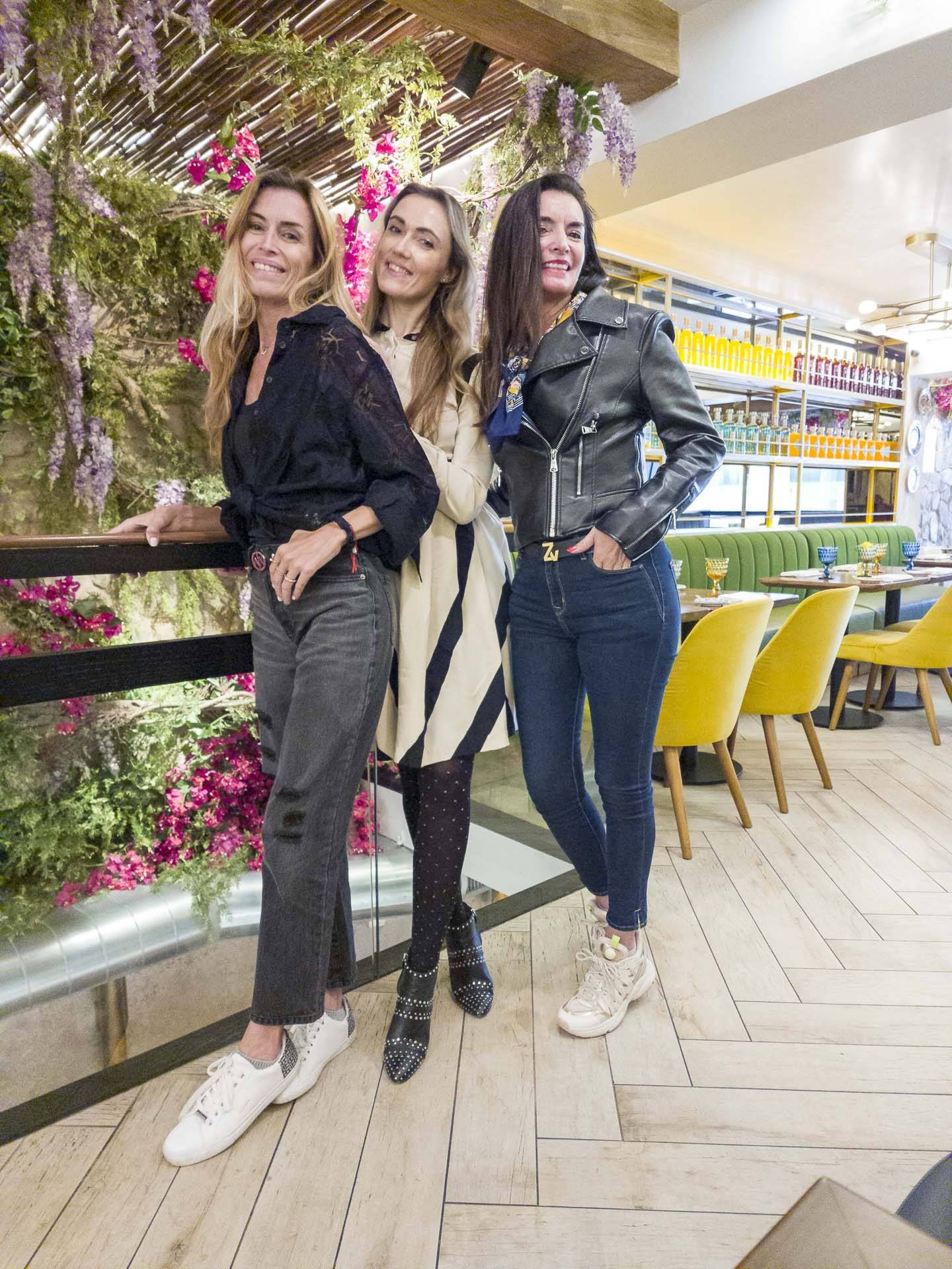 an image of three women standing in front of flowers at a cafe