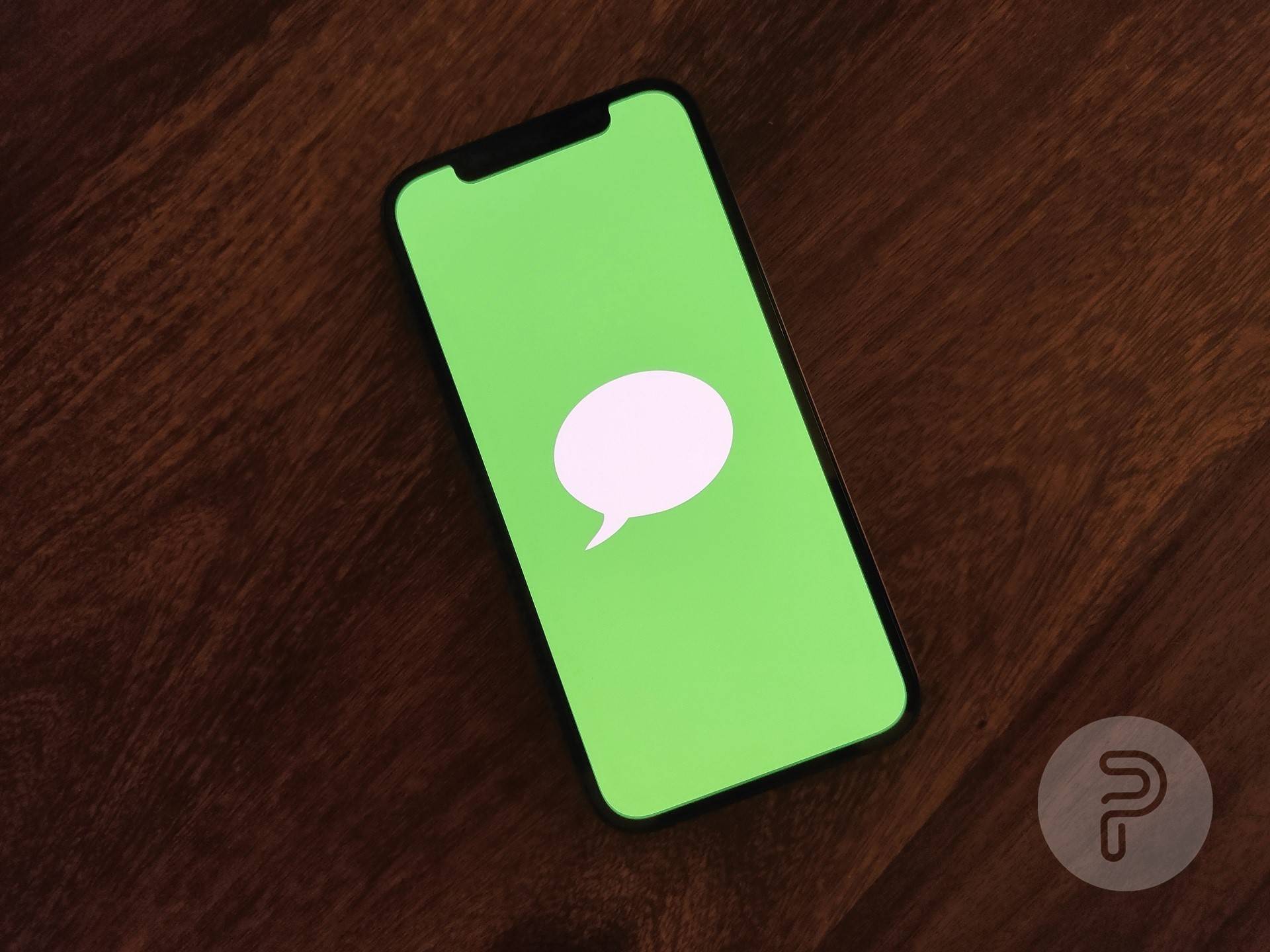 an iPhone placed on a table displaying an image with a green background and a chat bubble in the center